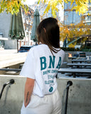 Person wearing a white t-shirt with 'BNA Brewing Company' text in an outdoor setting.