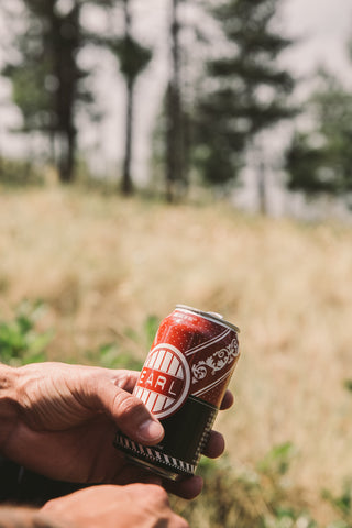 A photo of an "Earl" beer can. This is the name of our Pale Ale. The can is in someone's hand and the person is in a field with some trees. 